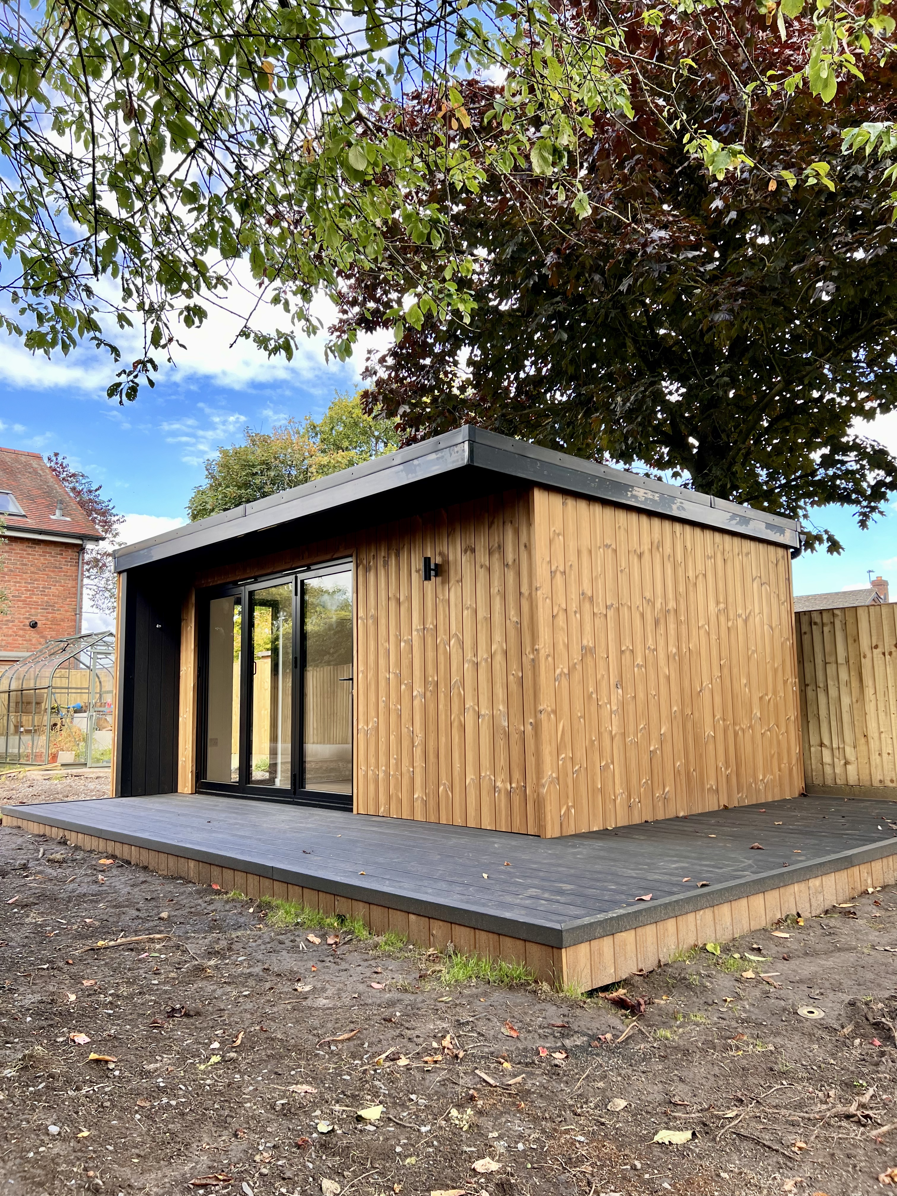 light wood clad large garden room with overhang and decking